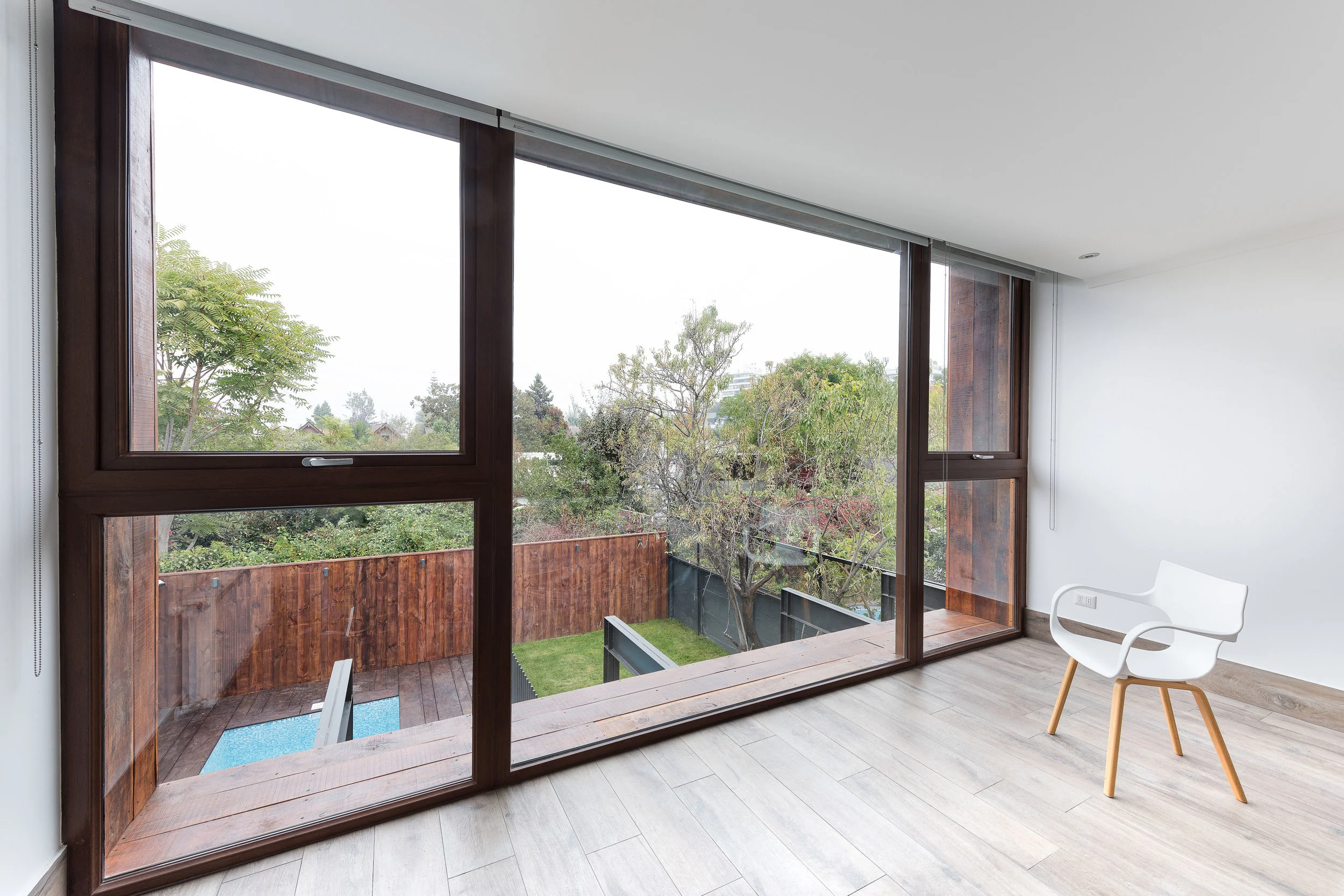 Interior con ventanal de marcos de madera que mira a un jardín con piscina
