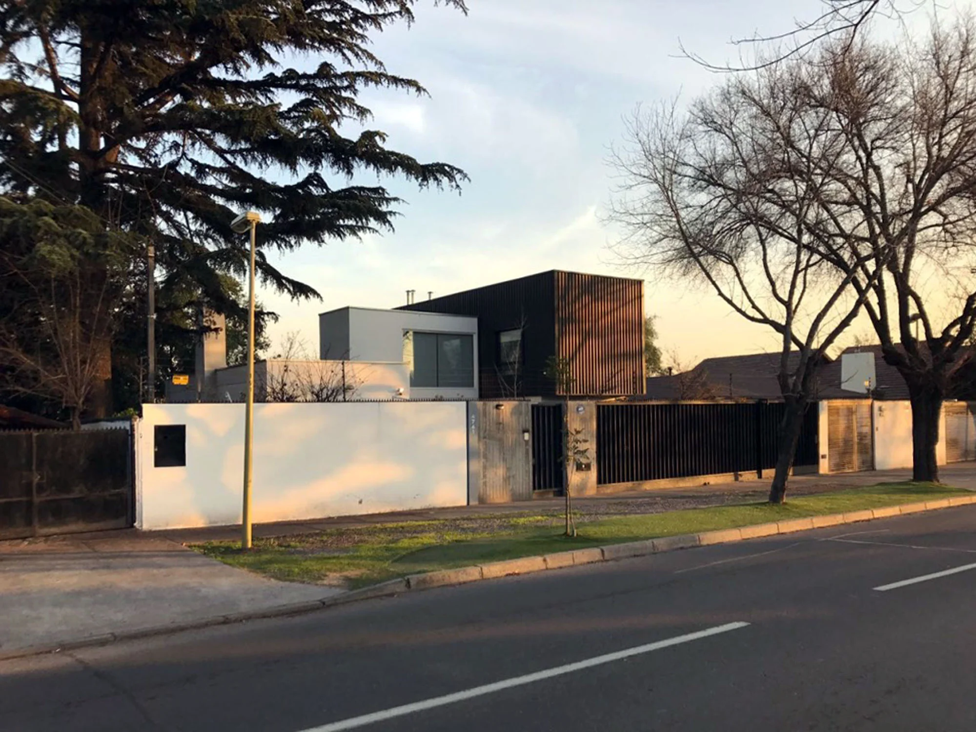 Casa de volúmenes blancos y negros con celosía de madera, vista desde la calle al atardecer